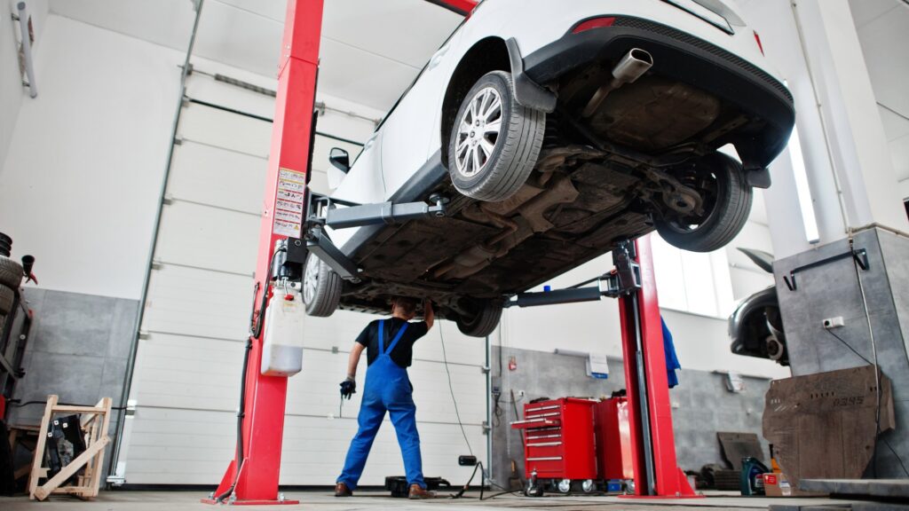 Car lifted on a hydraulic lift in a garage with a mechanic inspecting the underside.