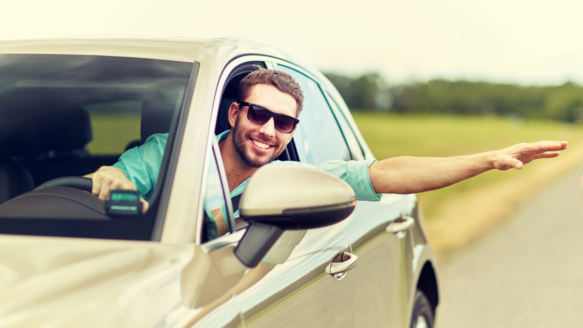 Smiling man wearing sunglasses leaning out of his car window while driving.